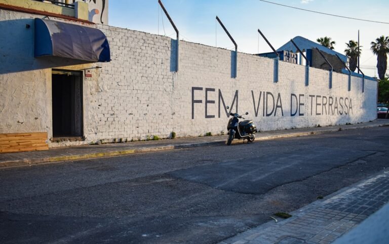vida em esparta - A scooter parked by a white wall with graffiti.